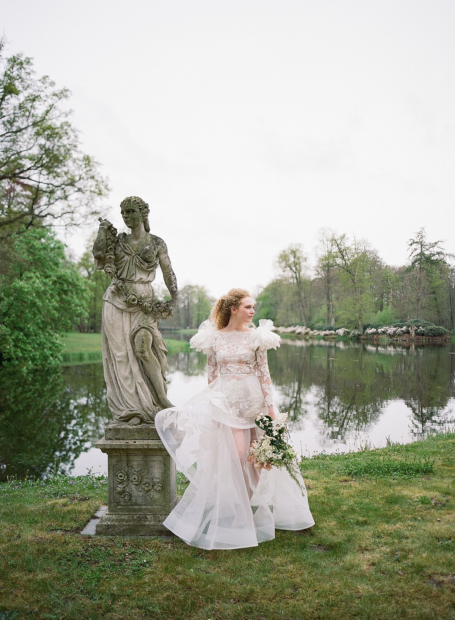 A garden scene with a classical stone statue beside a tranquil pond surrounded by spring greenery.