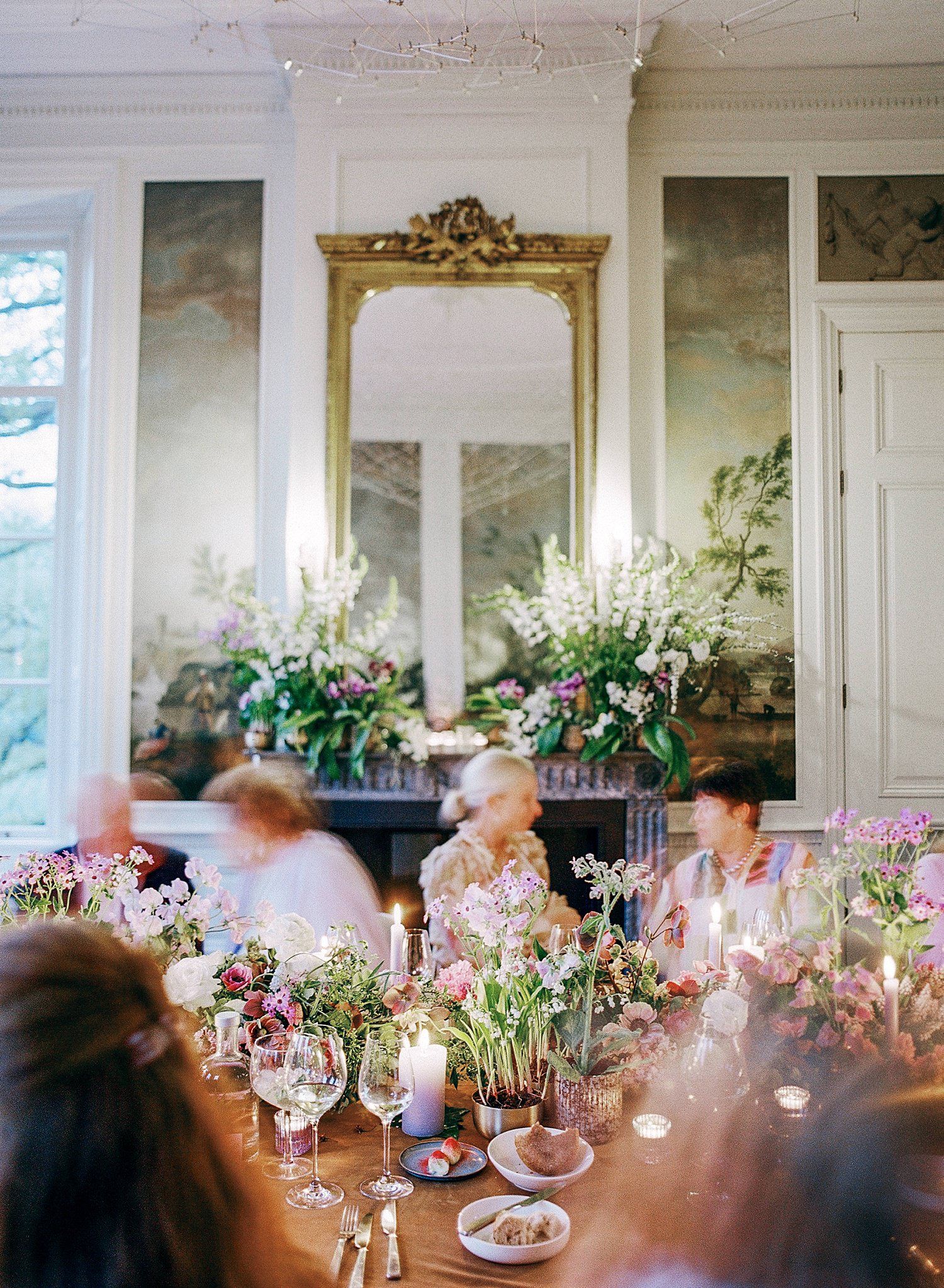 Elegant dining room with ornate gold mirror and floral centerpieces set for a formal gathering with wine glasses.