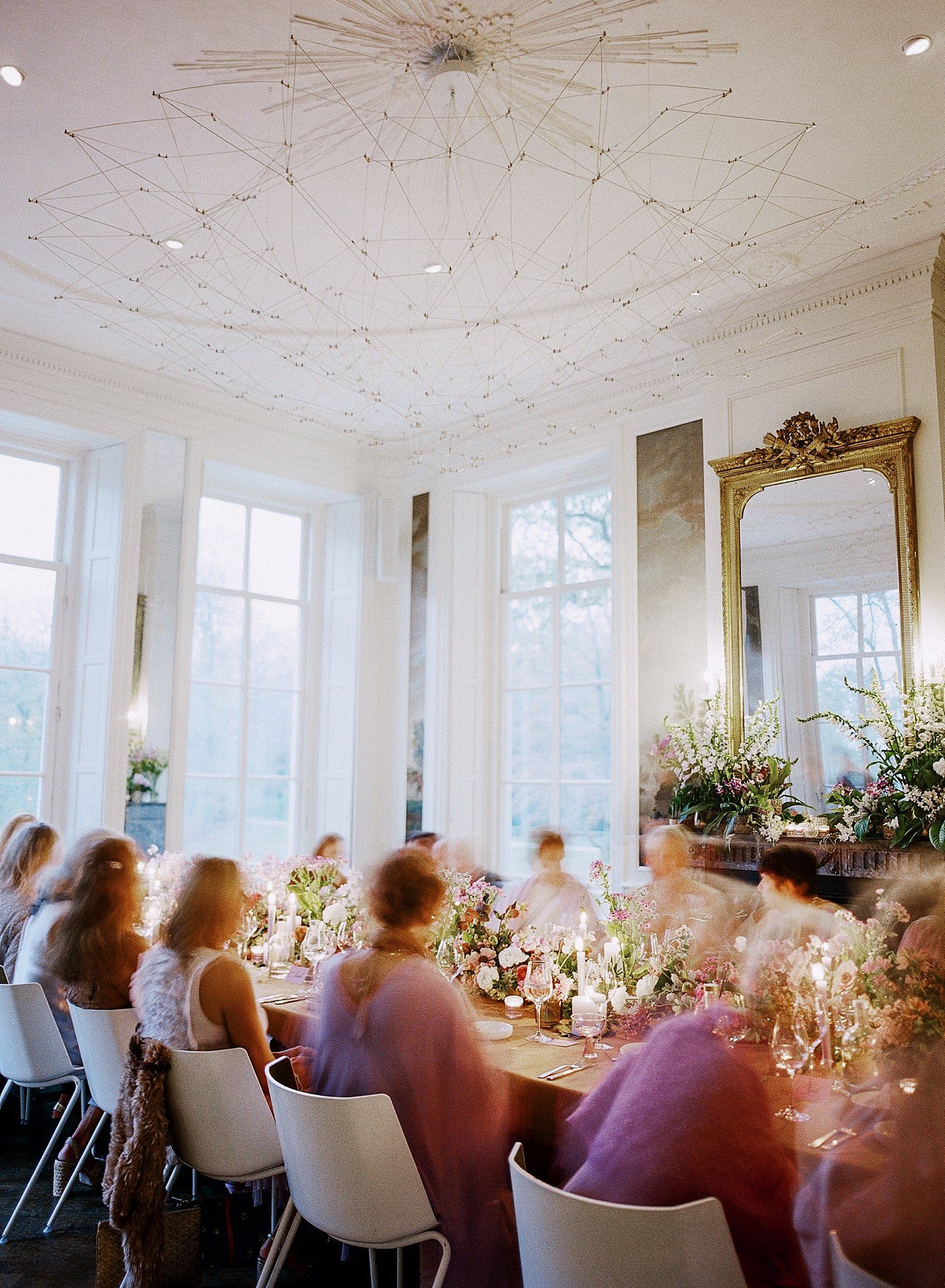 Elegant wedding reception venue with white ceiling, large windows, and long tables set for a formal dining celebration.