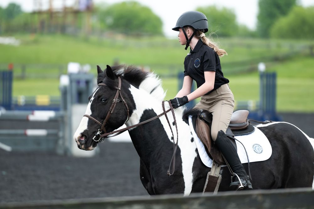 Equestrians in competition gear ride horses on an outdoor dressage course.