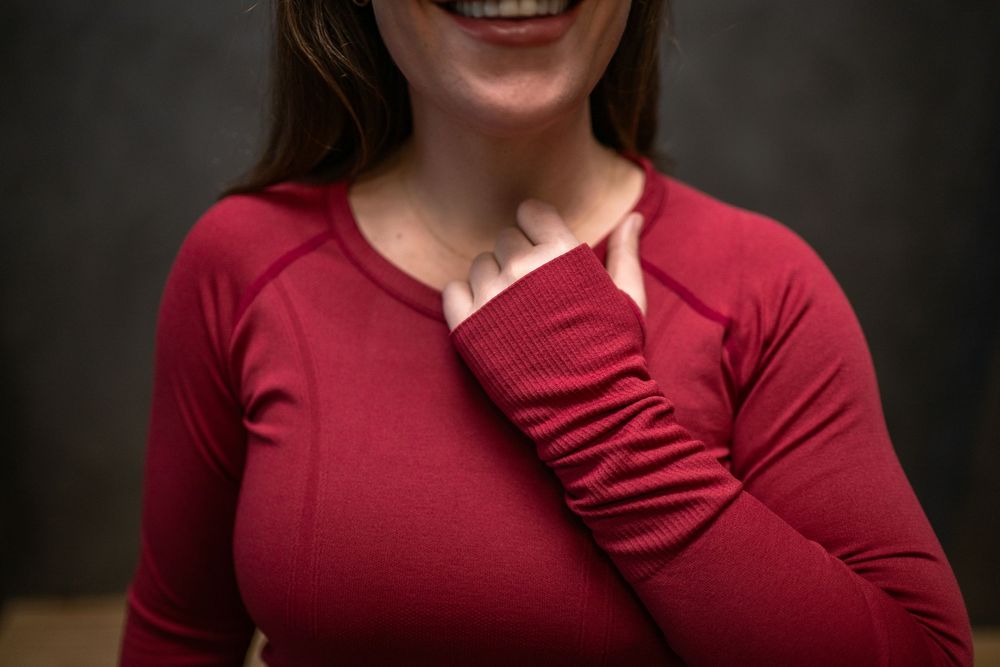 Woman wearing burgundy top smiling warmly against dark background.