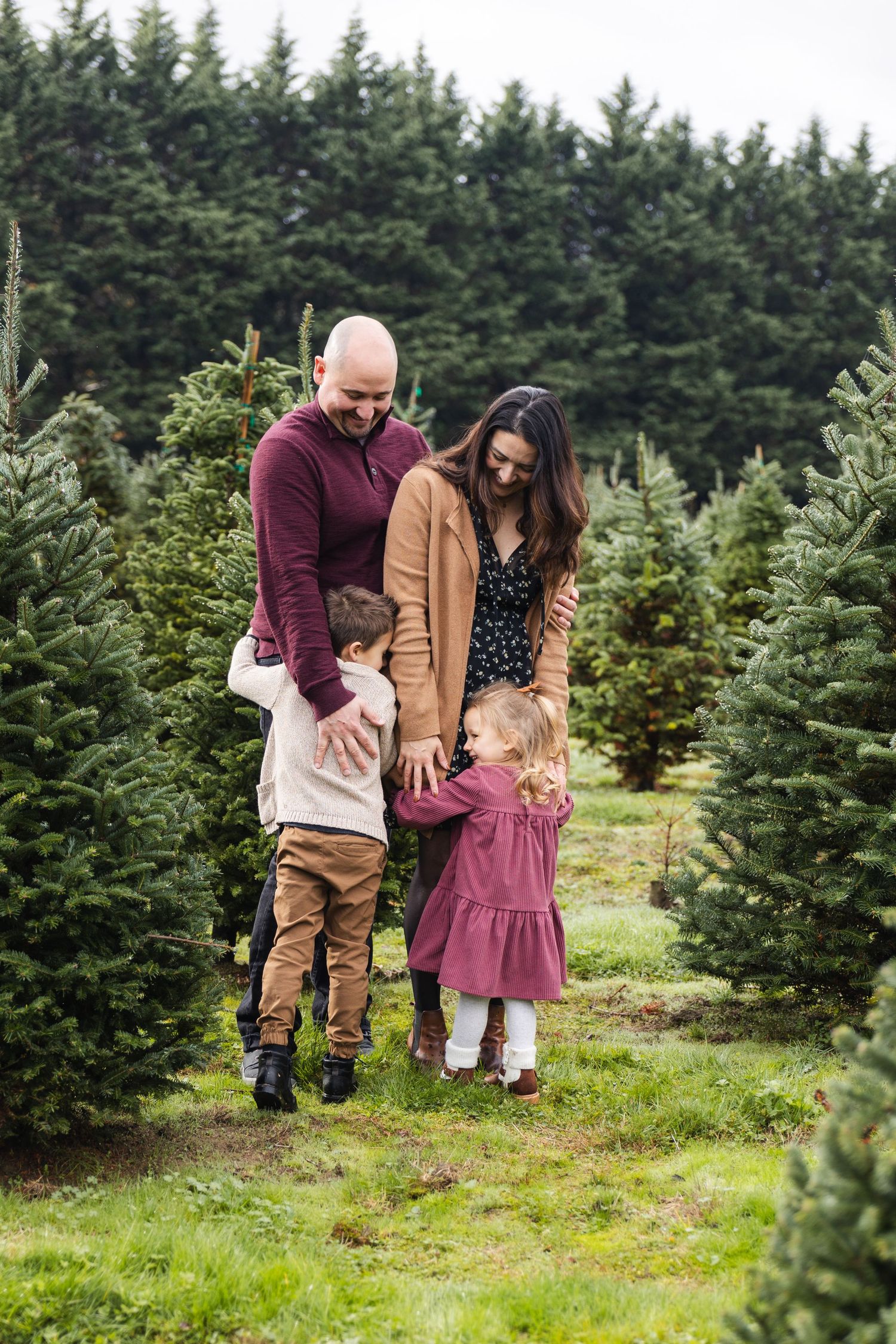 A family shares a tender moment together while visiting an evergreen Christmas tree farm on a cloudy day.