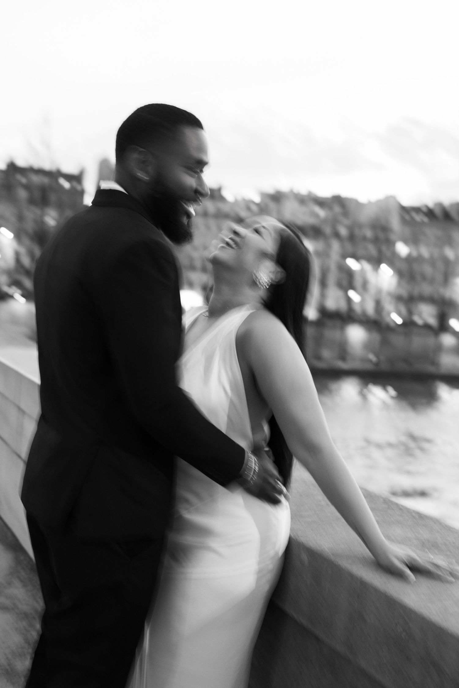 A romantic black and white wedding photo of a couple embracing by a waterfront, with the bride in a sleek white dress.