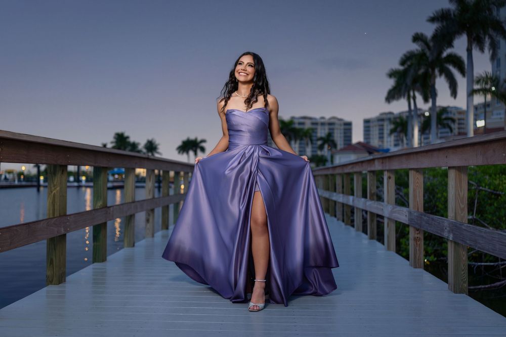 Young woman in flowing lavender ball gown posing on wooden boardwalk at twilight in Florida.
