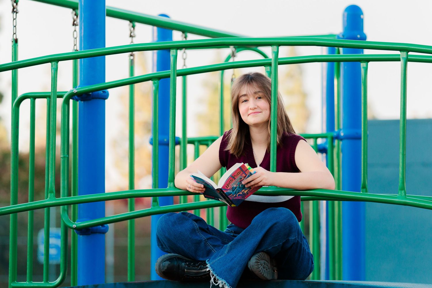 Someone reads a book while sitting on colorful playground equipment on a sunny day.