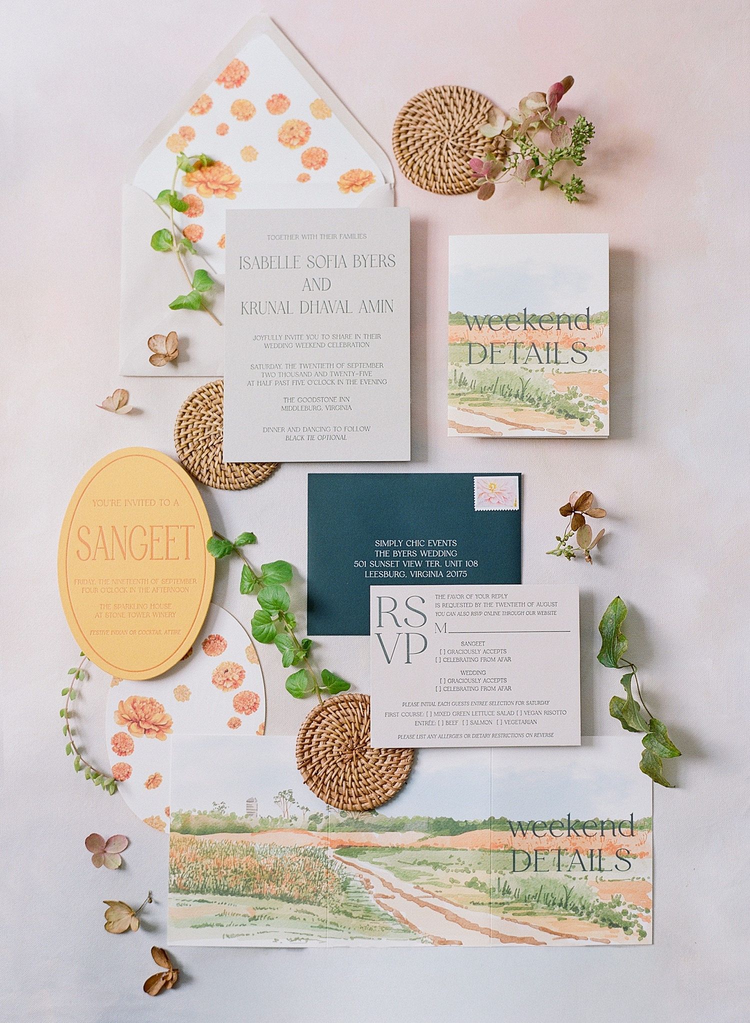 Elegant wedding invitation suite with watercolor landscape design, coral florals, and gold accents laid out on light background.