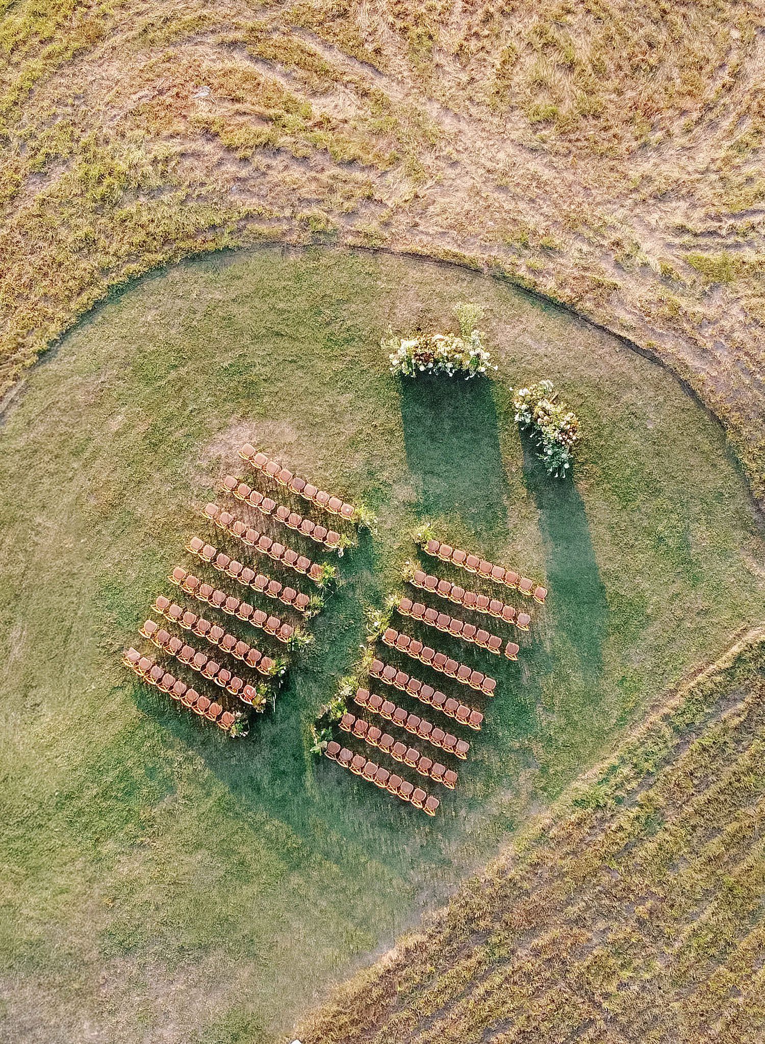 Aerial view of wooden benches arranged in rows on a circular green lawn surrounded by dry grassland.