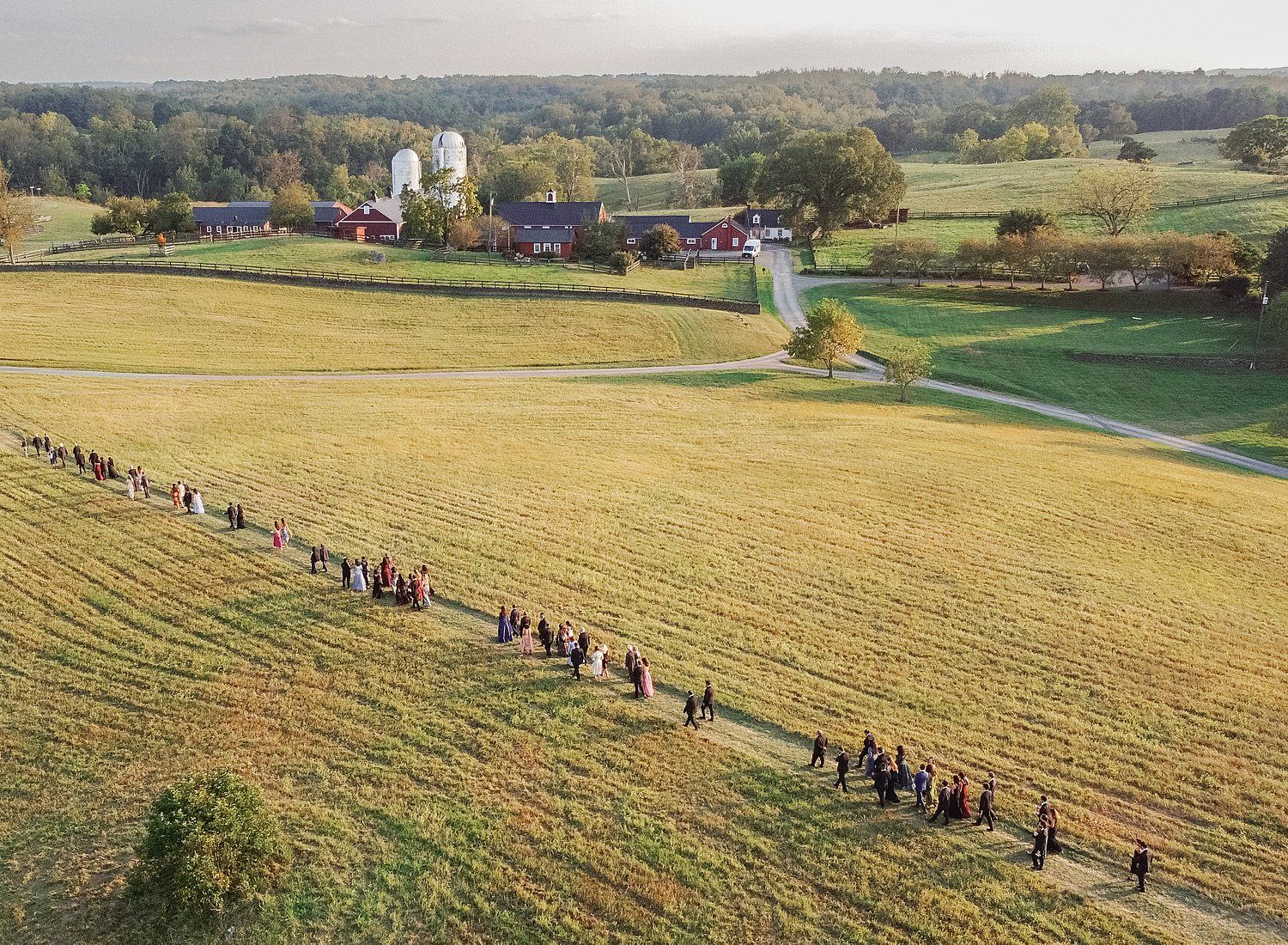 Aerial panoramic view of a group walking through golden autumn fields during harvest season.