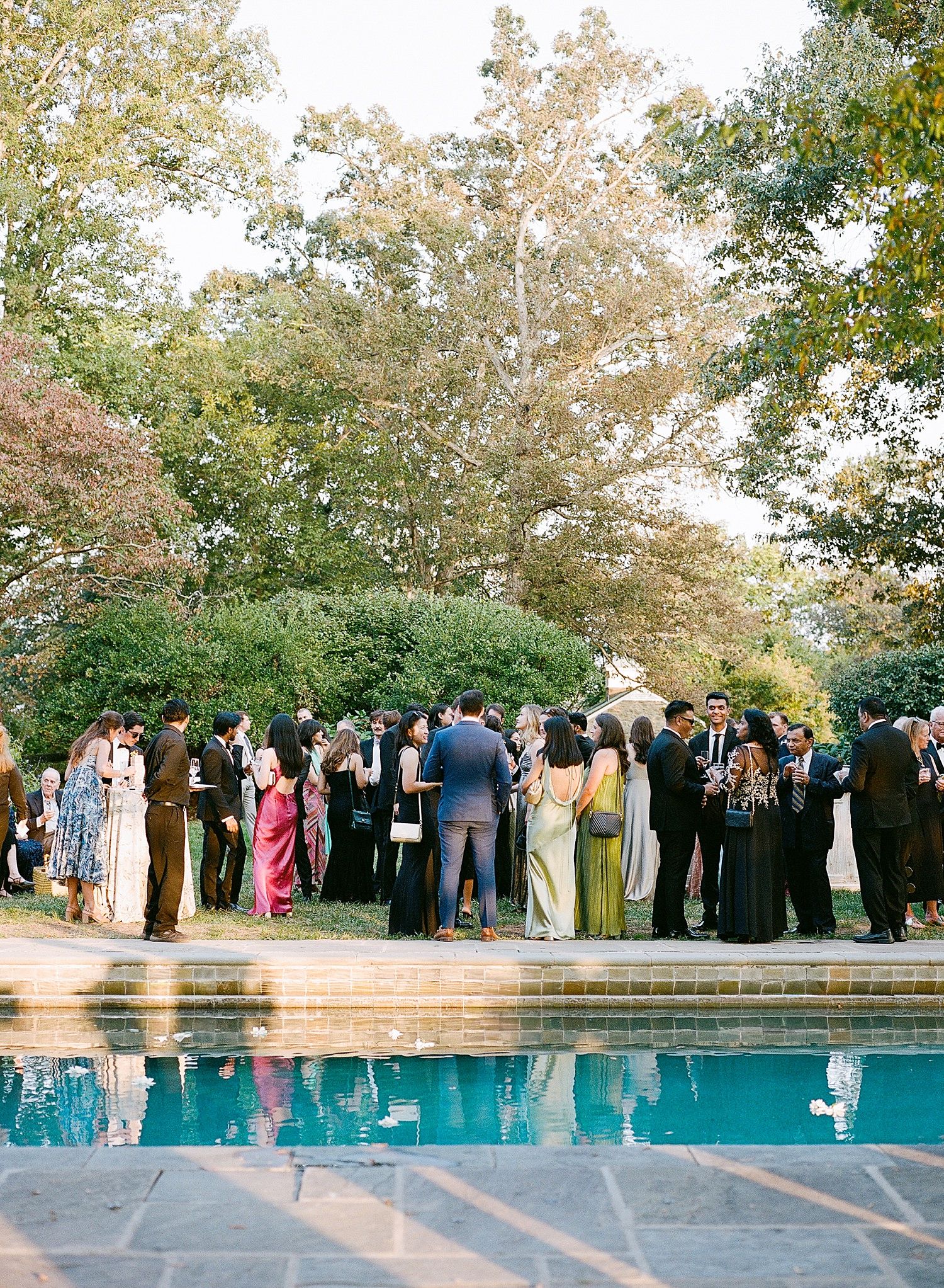A panoramic view of wedding guests gathered around an elegant outdoor pool during a formal celebration.