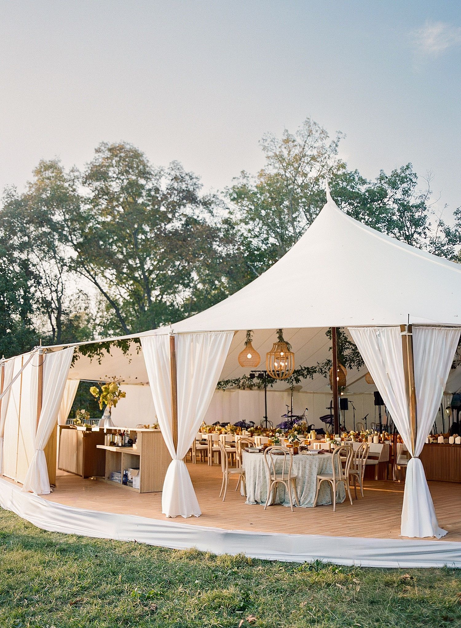 Elegant outdoor wedding tent setup with flowing white drapes and natural landscaping in a garden setting.