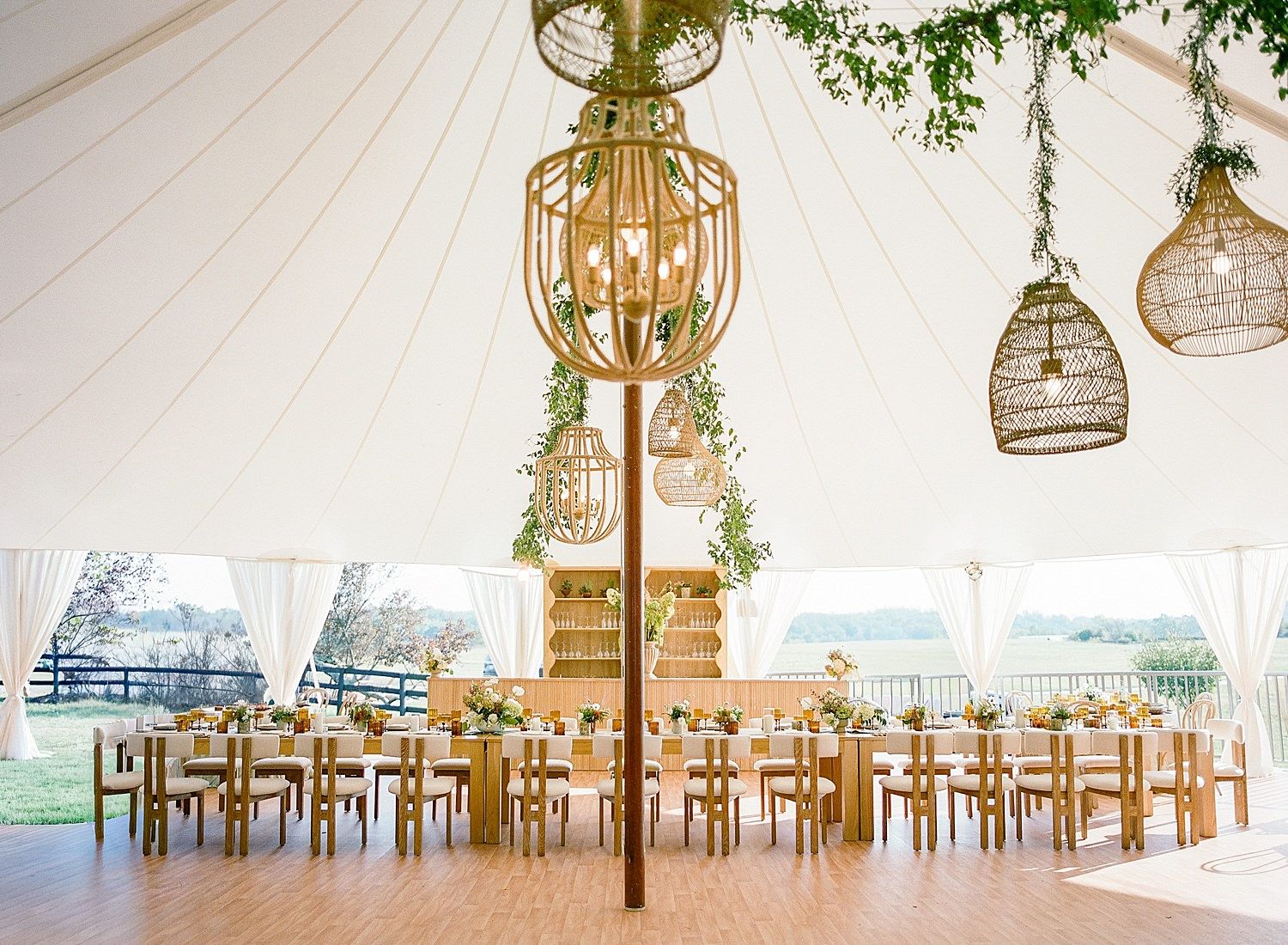 Elegant wedding venue with rustic chandeliers and wooden tables set for a reception under a white tent.