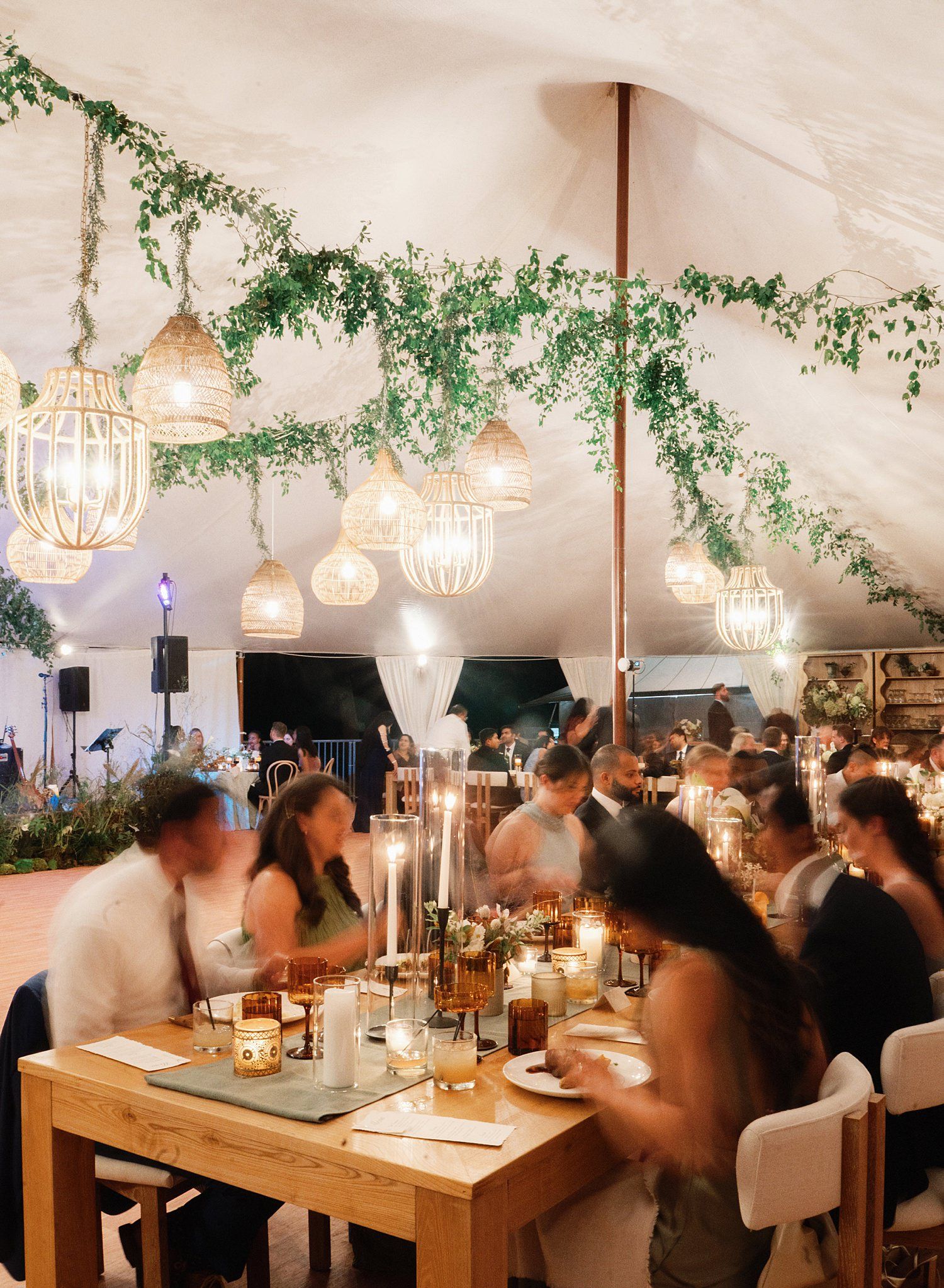 Elegant wedding reception venue with hanging crystal chandeliers, greenery decor, and wooden dining tables in a white tent.