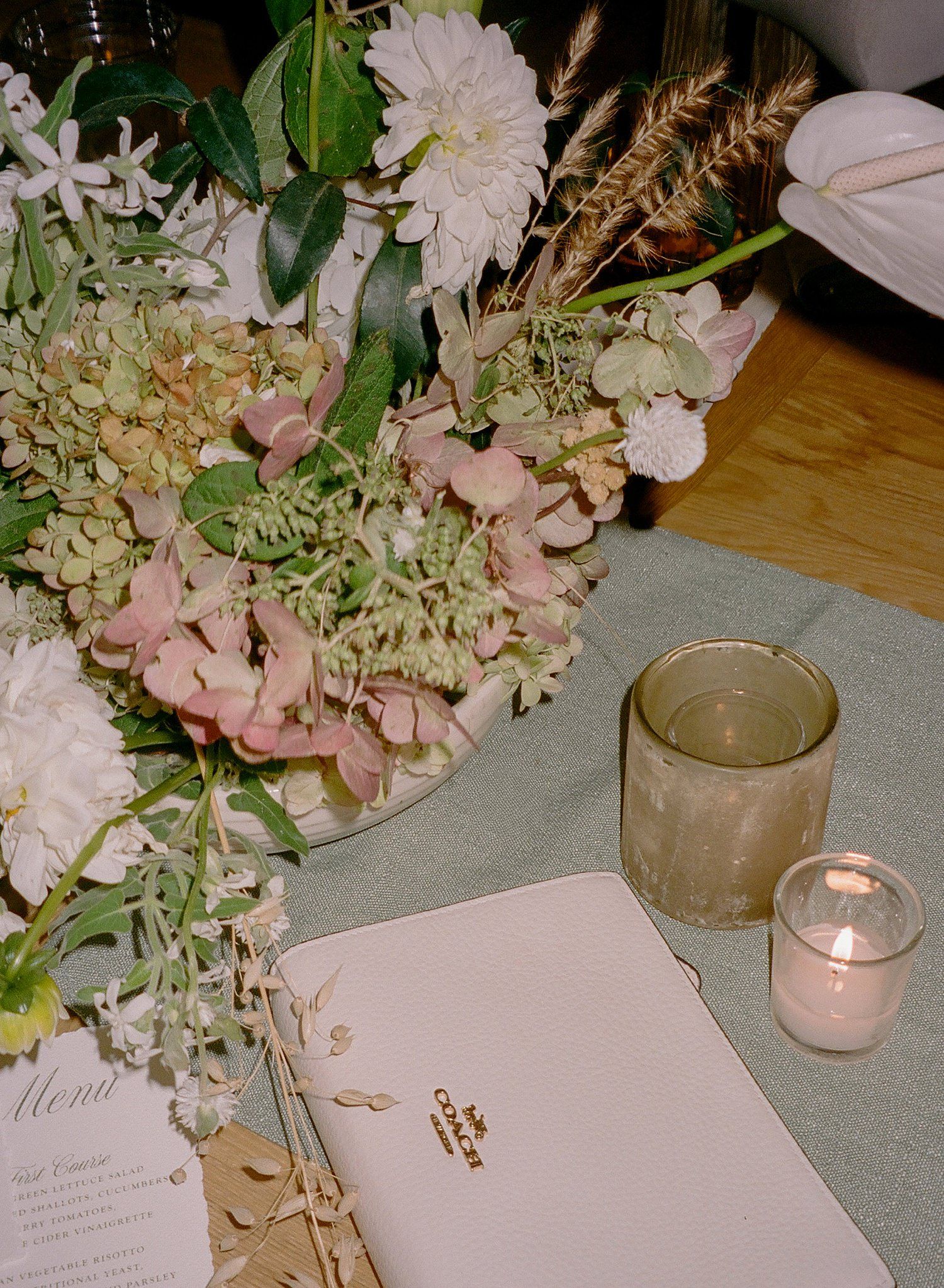 Elegant wedding reception table setting with pink and white hydrangeas, candles, and menu cards on a light tablecloth.