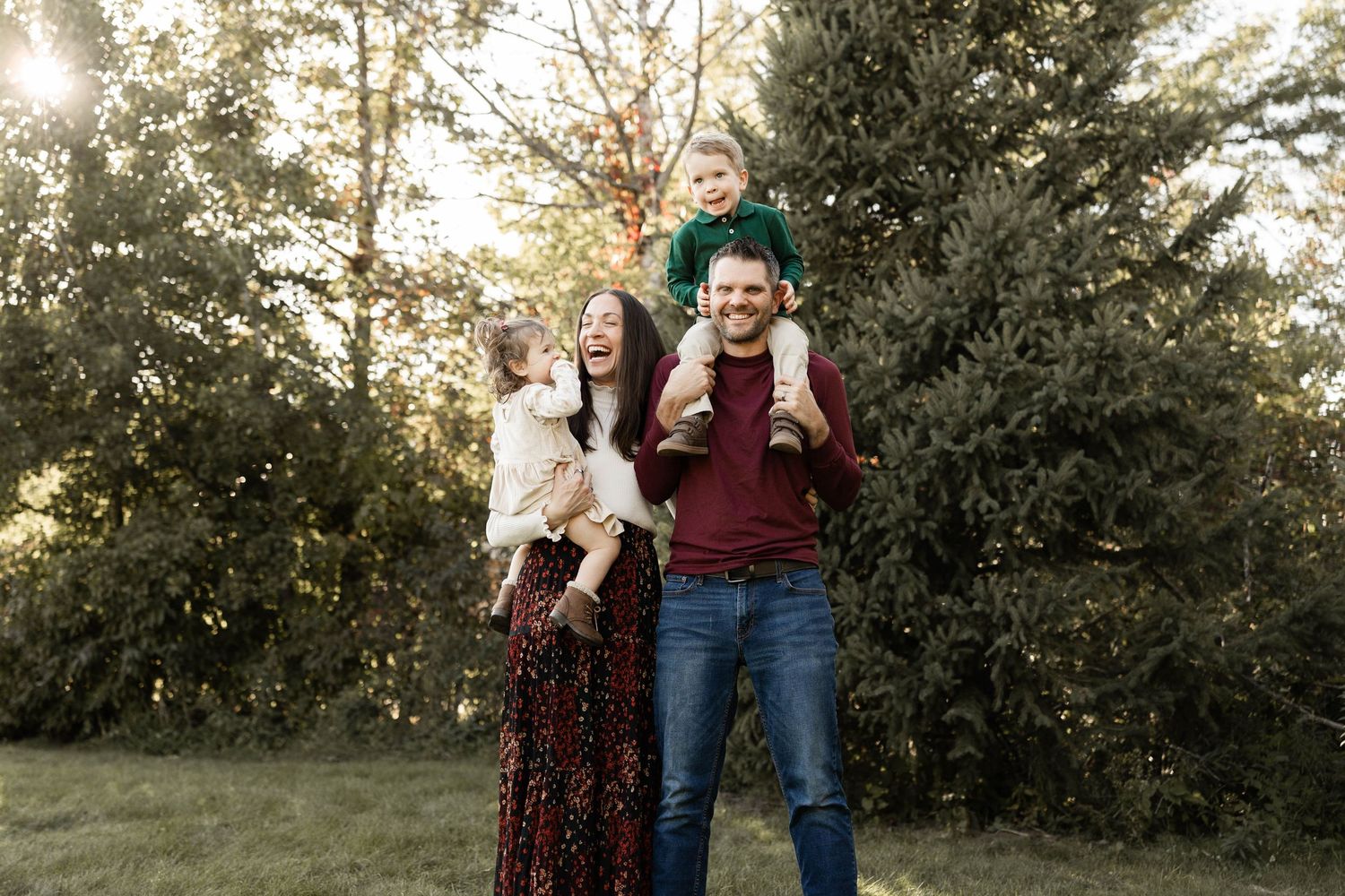 A group stands together outdoors at sunset with evergreen trees in the background.