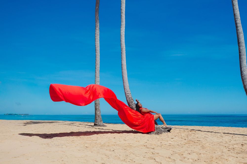 A bright red hammock sways between palm trees on a pristine tropical beach with turquoise ocean waters.