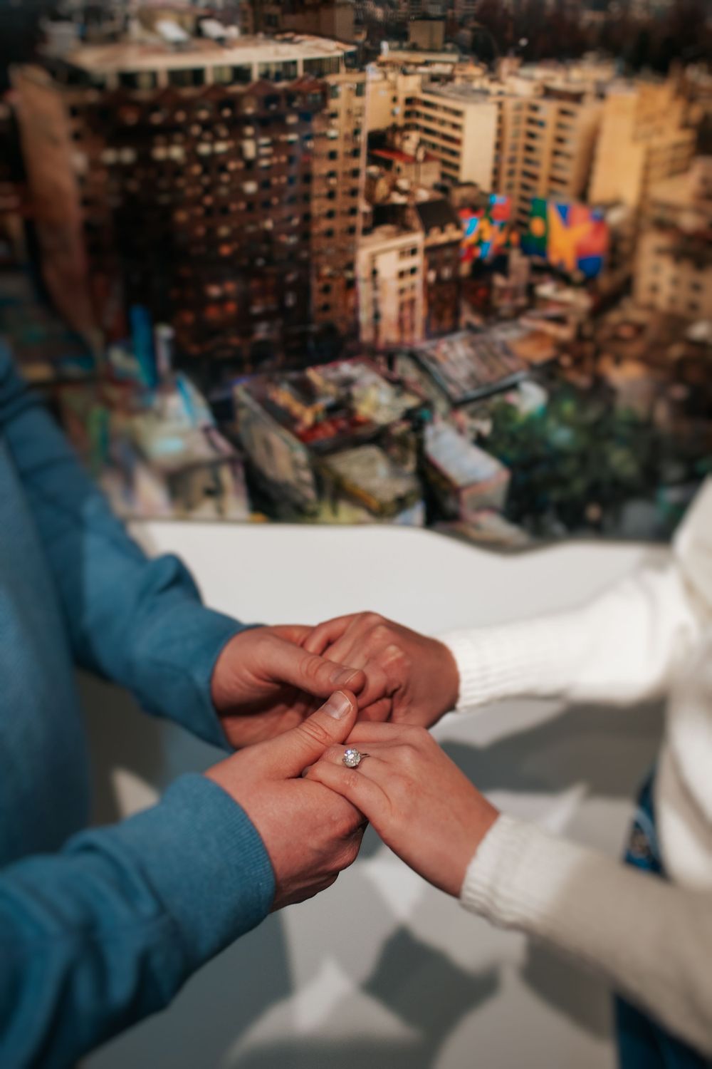 Close-up of hands exchanging rings against a blurred cityscape background.