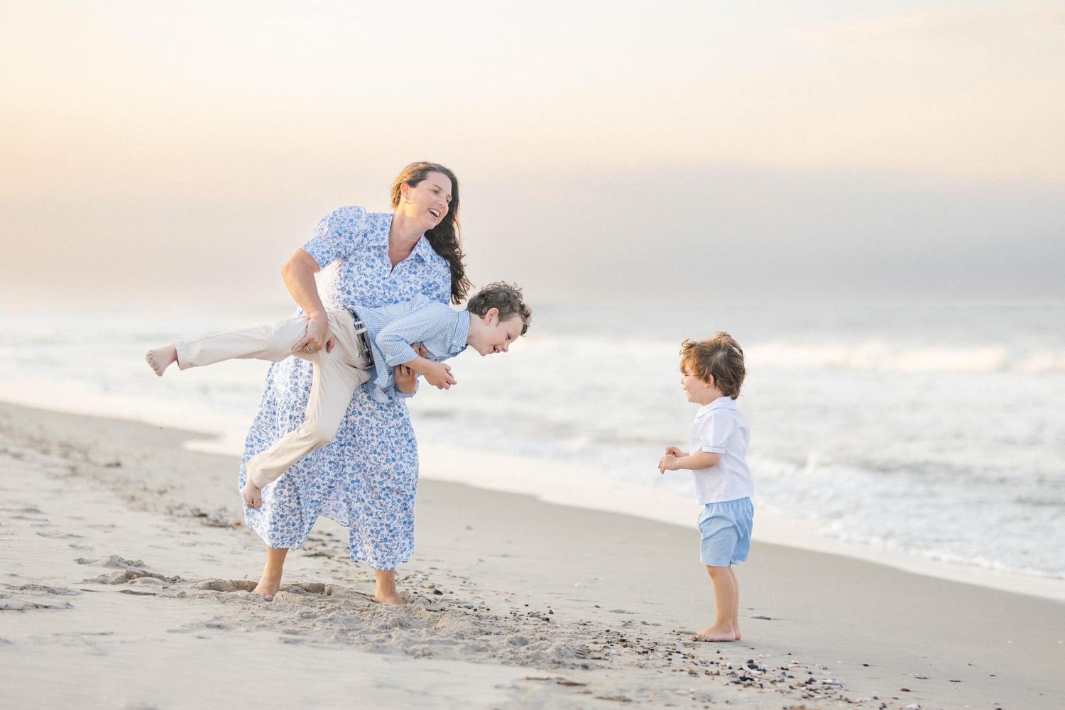A family plays together on a sandy beach at sunset wearing coordinated blue and white outfits.