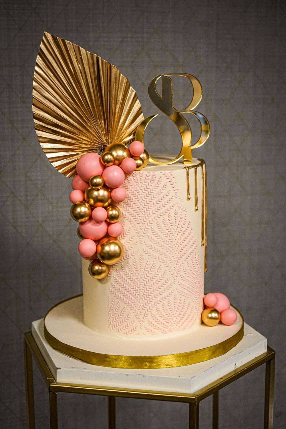 Modern white wedding cake decorated with gold fan details and coral pink and gold baubles.