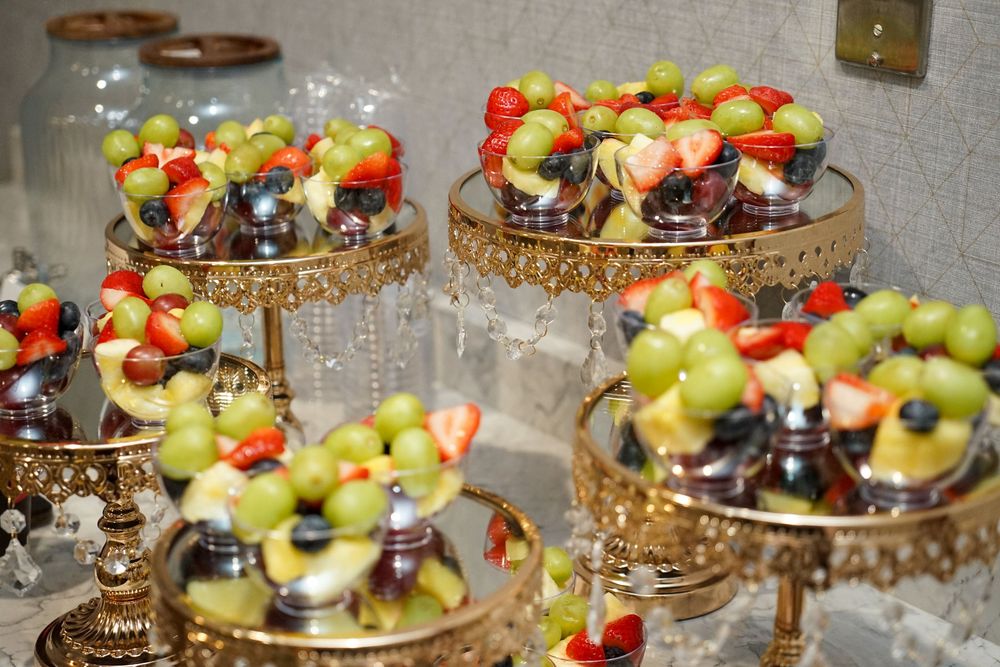 Elegant display of fresh fruit cups on gold tiered stands at catering event.