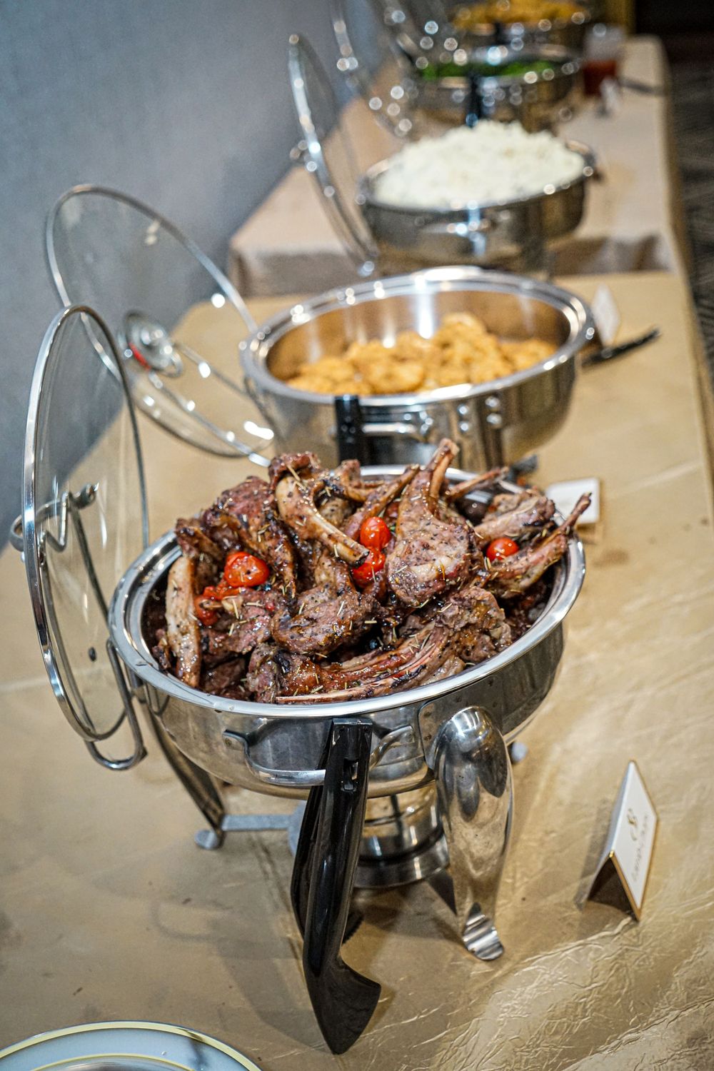 Chafing dishes filled with grilled meats and savory dishes at a catered buffet.