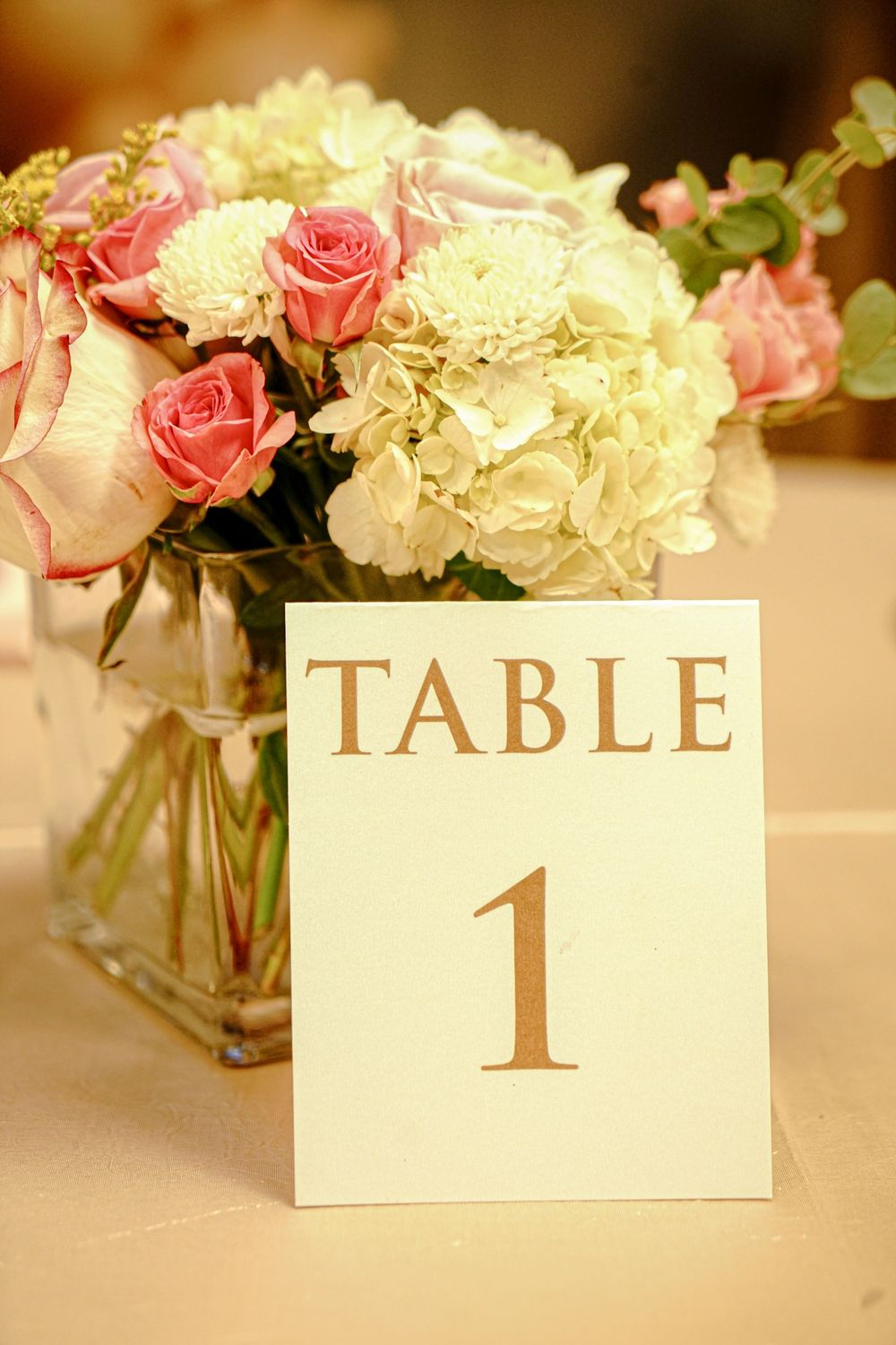 Elegant wedding table setting with pink roses, white hydrangeas and gold table number card.