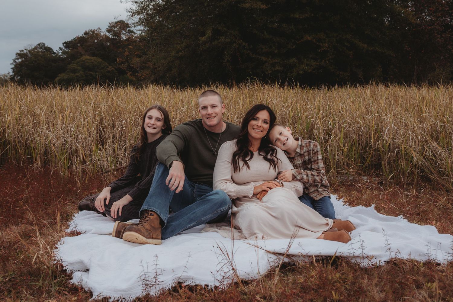 Cullman Alabama Family Photographer. People sit together on a white blanket in a golden autumn field during sunset.