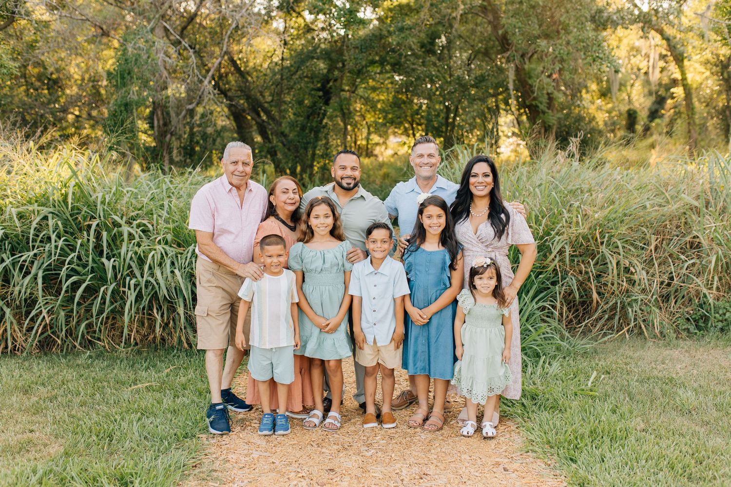 Extended family standing together outdoors under a large tree.