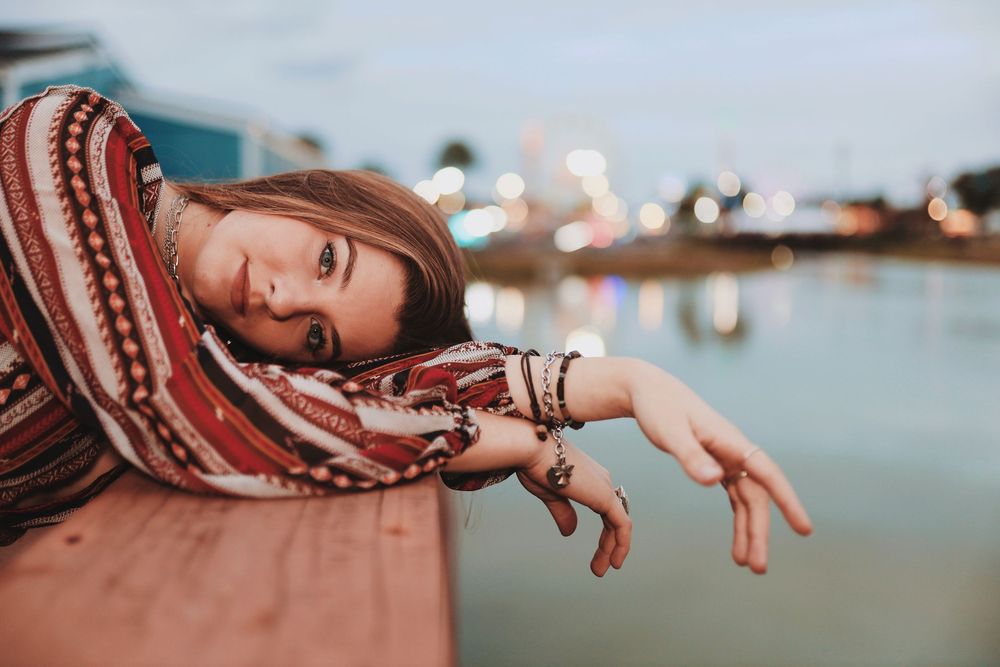 Person wearing a brown and white striped sweater poses against a blurred background with soft bokeh lighting.