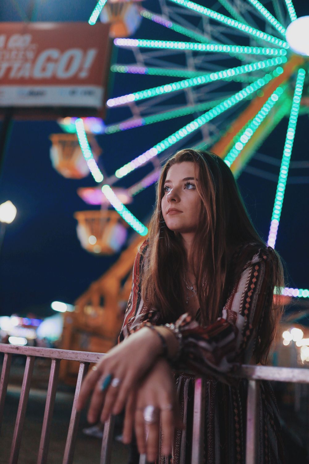 Colorful carnival lights illuminate a nighttime scene at an amusement park with glowing neon ferris wheel spokes in background.