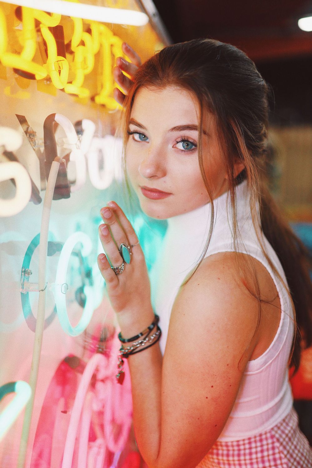Portrait against neon lights showing a casual look in pink tank top with gingham pattern details.