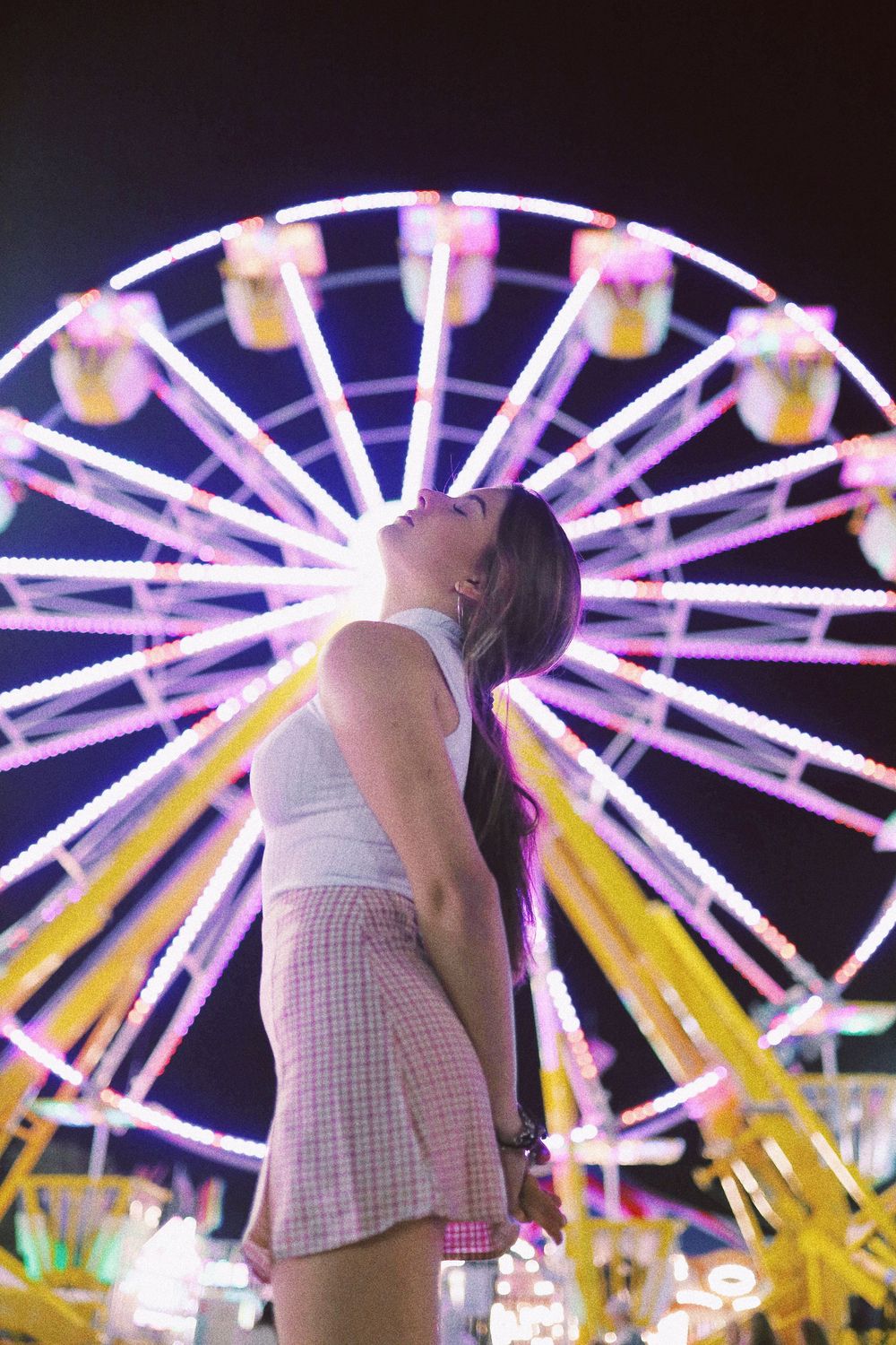 A sequence of photos showing a person in white clothing dancing with a colorfully lit ferris wheel in the background.