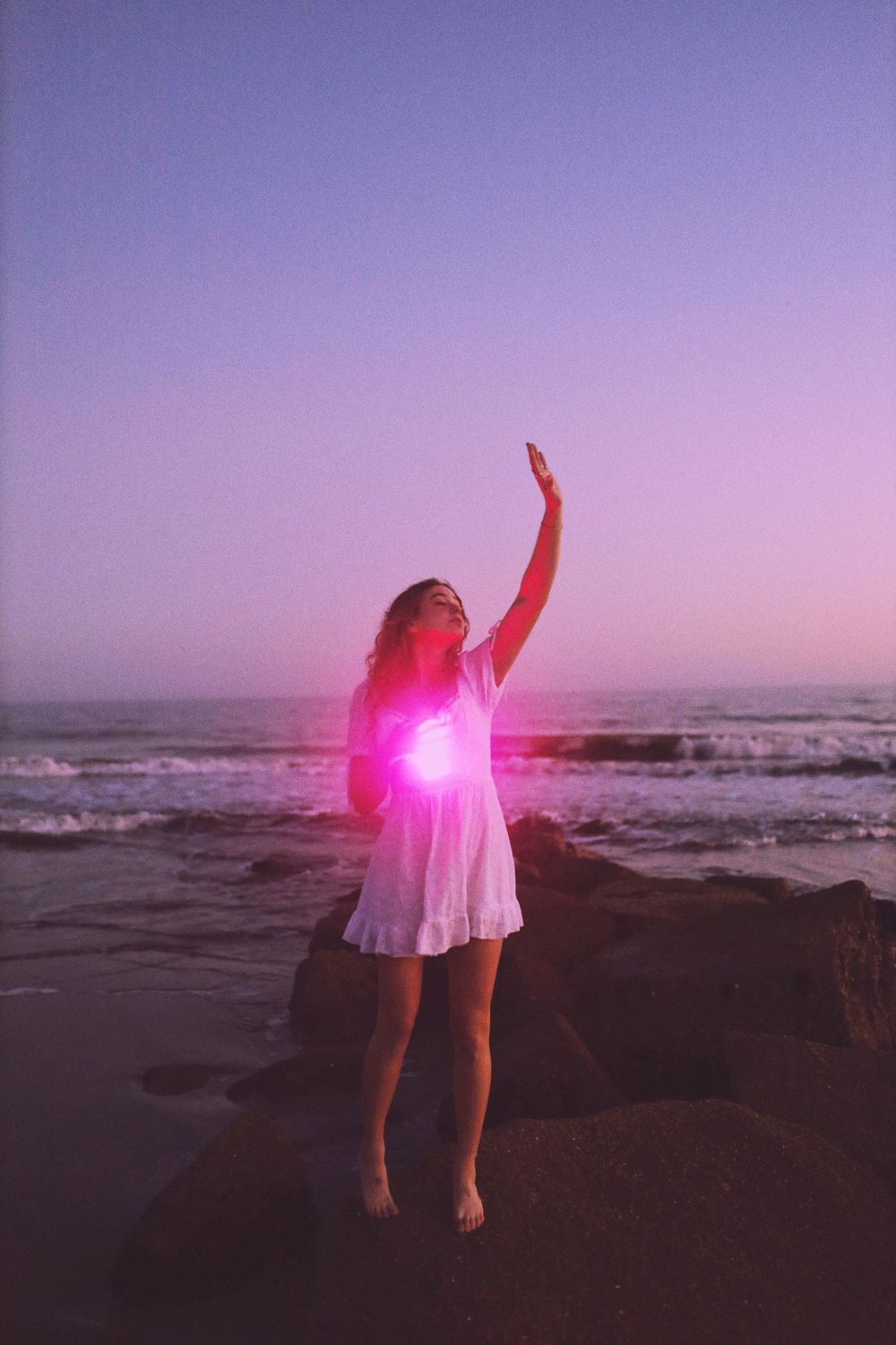 A person dances on a beach at sunset with a pink glow effect creating a dreamy silhouette against the ocean backdrop.