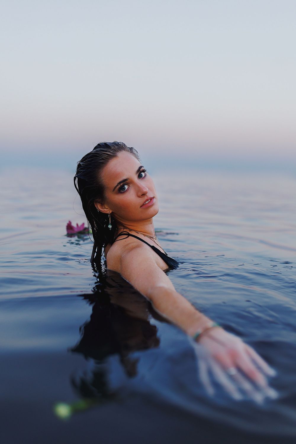 A person floats in calm blue water at dusk with their arm outstretched.