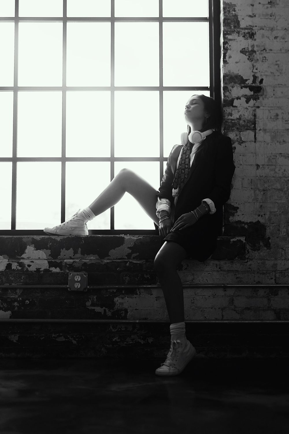 A black and white image shows a person sitting on a windowsill in a warehouse-style space with large windows.