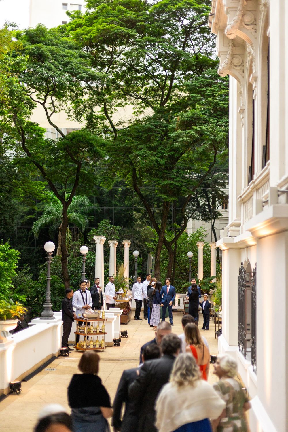 Elegant outdoor wedding ceremony setup with white columns and lanterns along a tree-lined path.
