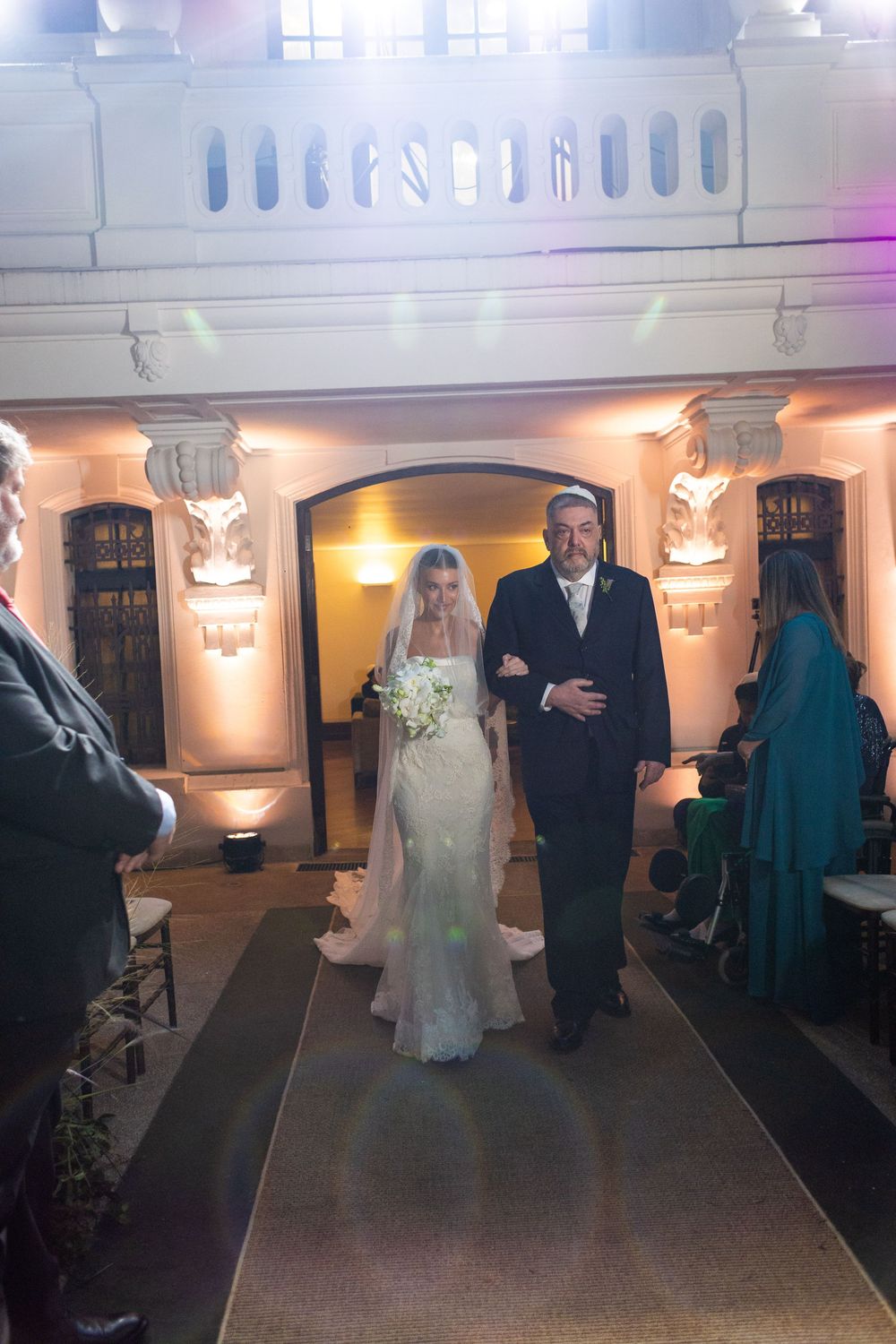 Wedding processional in a beautifully lit indoor venue with decorative wall sconces.