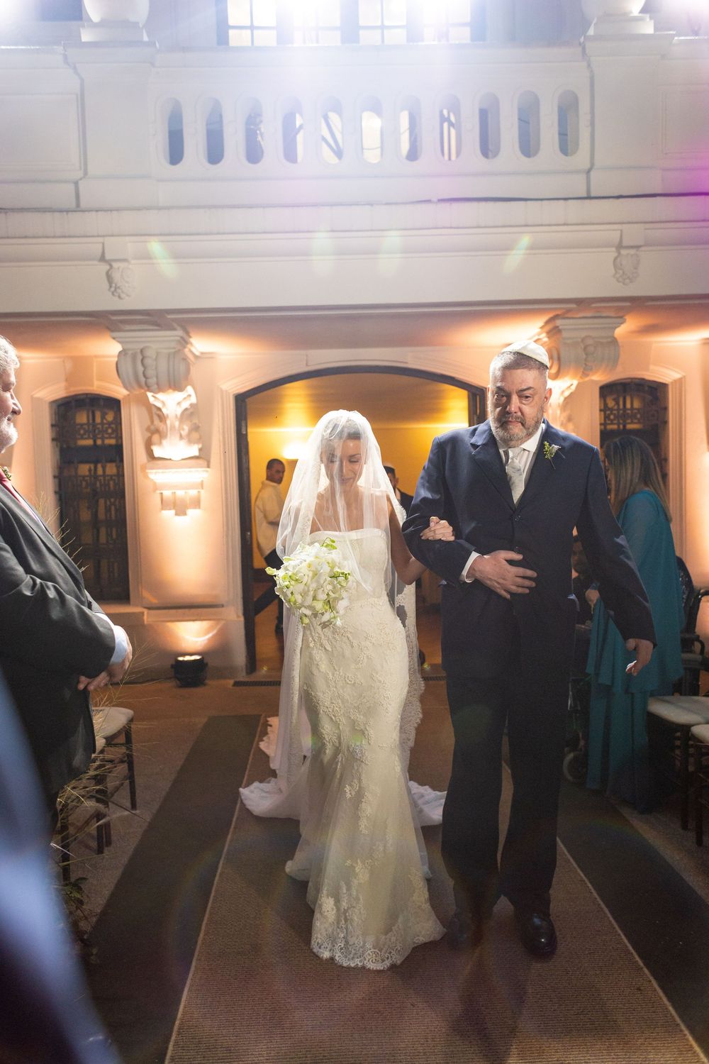 A wedding processional in an elegant indoor venue with ornate architectural details.