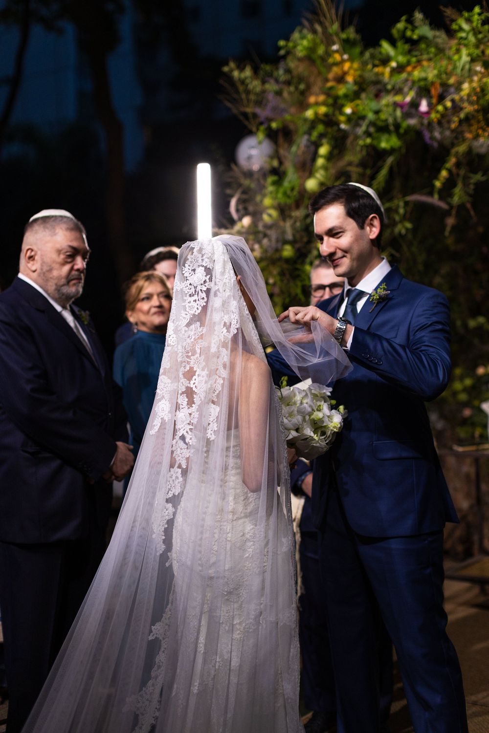 A wedding ceremony in a garden setting with participants gathered around a glowing light fixture.