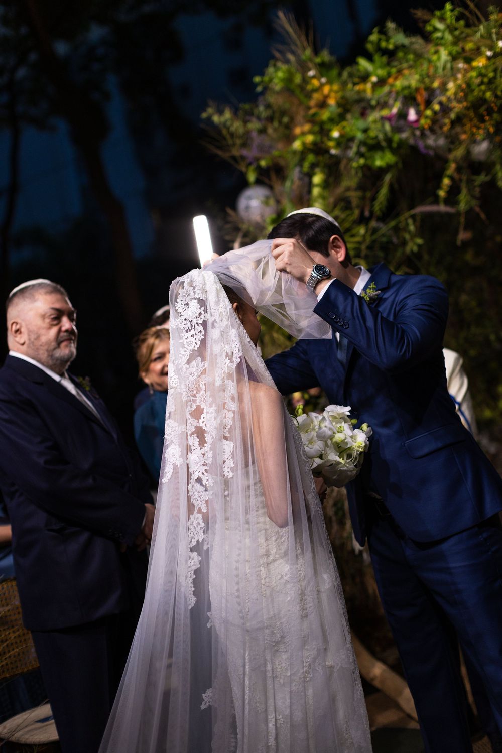 A romantic wedding moment captured under a floral arch during an evening ceremony.