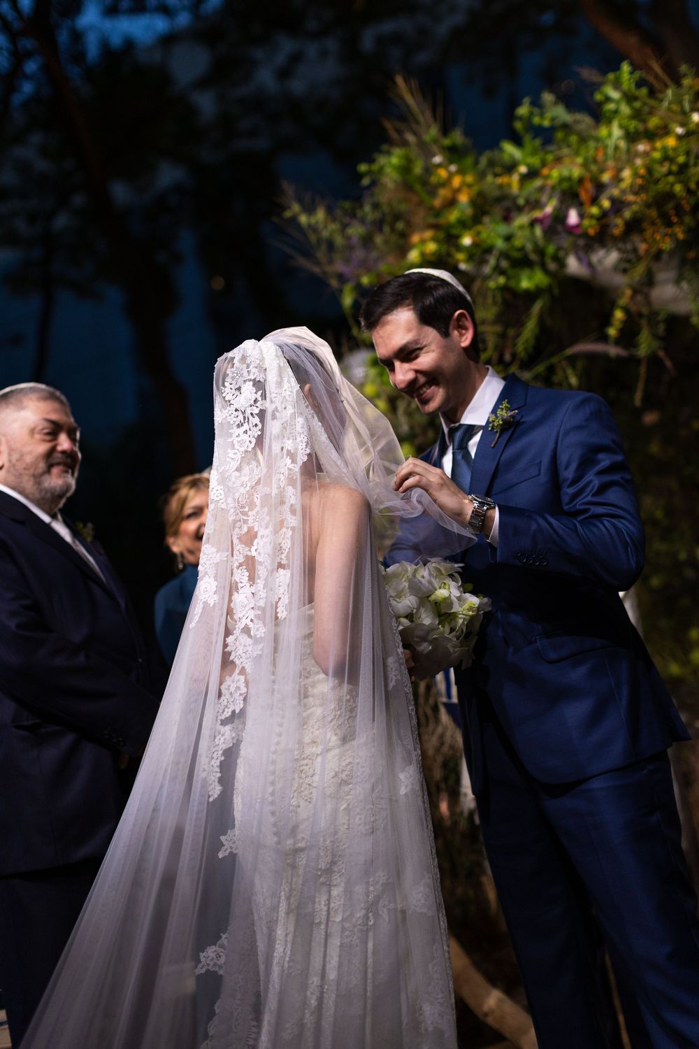 A wedding ceremony under a floral arch with traditional Jewish ceremonial elements.