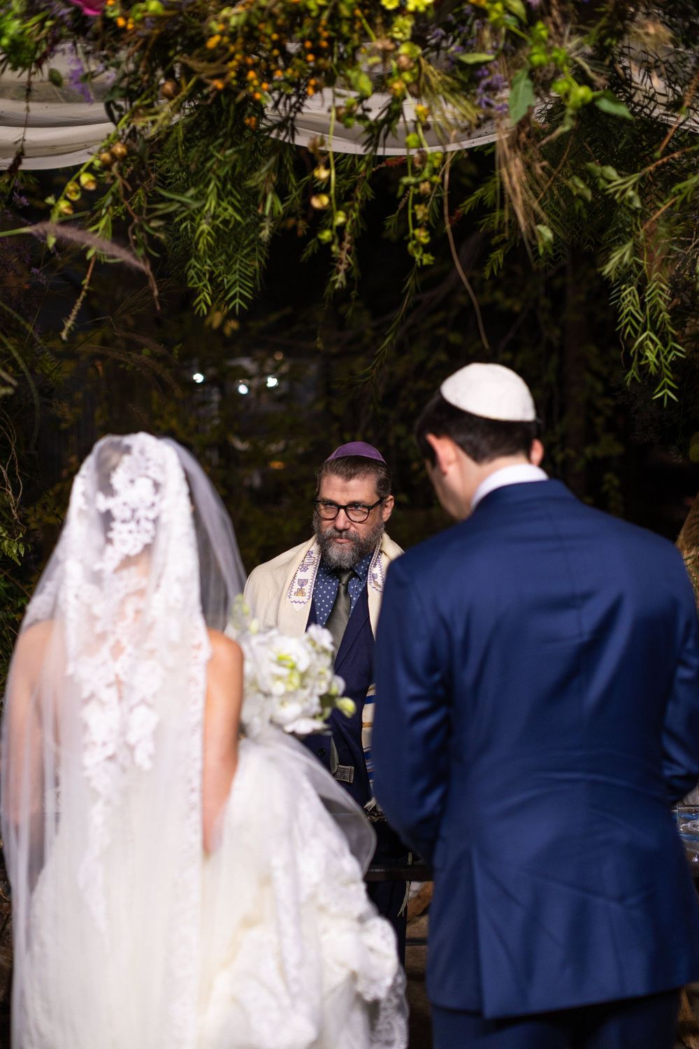 Outdoor wedding ceremony under natural foliage with traditional Jewish customs being performed.
