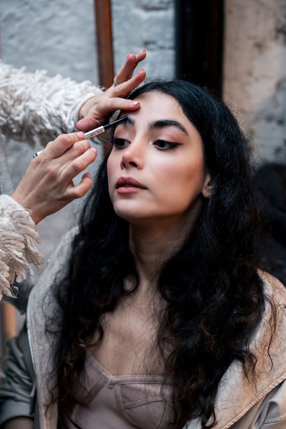 Behind-the-scenes makeup application showing dramatic eye makeup and curly dark hair.