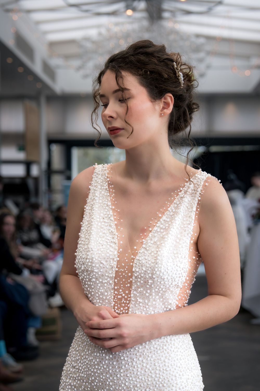 A bride in a white pearl-embellished wedding dress poses in an indoor venue.