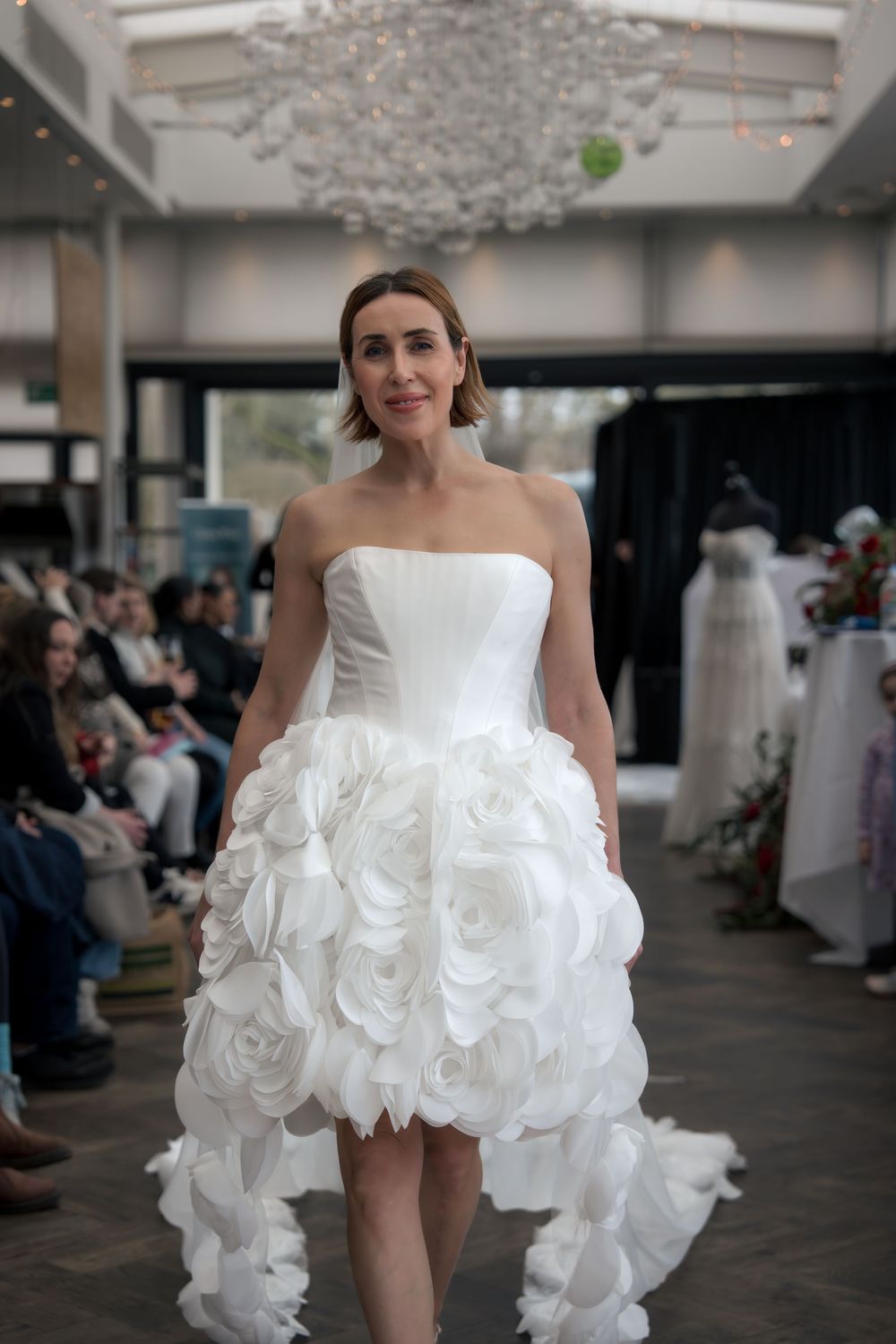 A fashion show features a white ruffled wedding dress design with dramatic layered details on display.