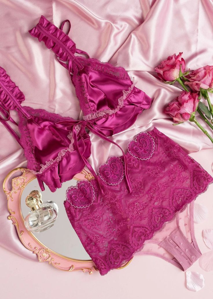 Fuchsia lace lingerie set laid out on pink satin fabric with delicate floral embellishments and ruffled details.
