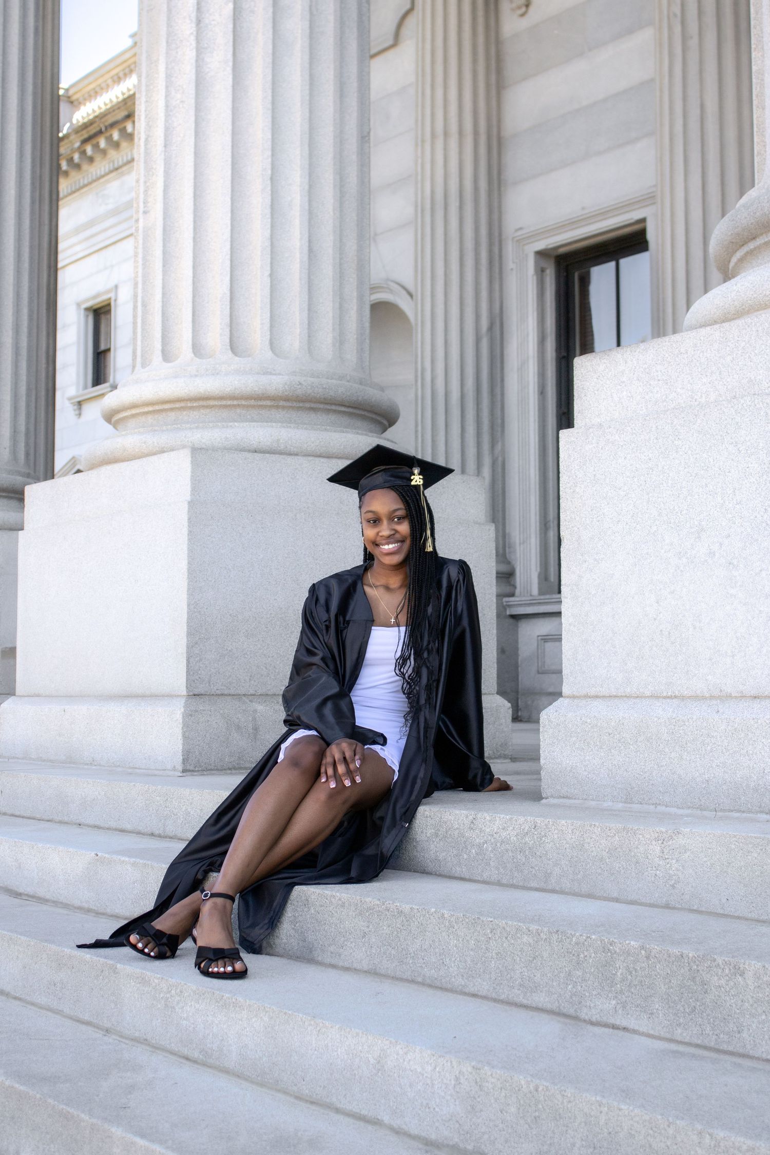Graduate in cap and gown poses on marble steps of classical building in creative portrait series.