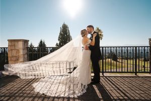 A couple shares a romantic moment on a sunlit balcony with a long flowing wedding dress veil catching the light.