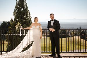 A wedding couple stands on a balcony overlooking a scenic mountain landscape during golden hour.