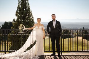 A wedding couple stands on a scenic overlook with mountain views and a wrought iron railing in the background.