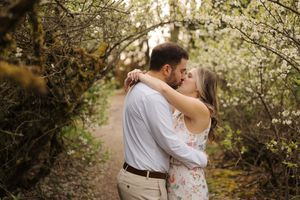 A couple embraces in a romantic moment surrounded by blooming spring trees and natural light.